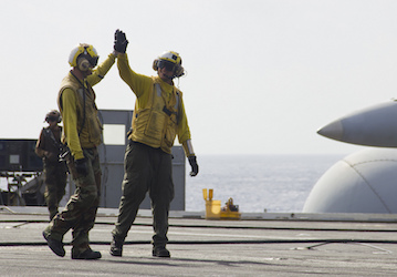 Sailors wearing protective gear high-five on flight deck after an aircraft launch show that teamwork improves performance  US
