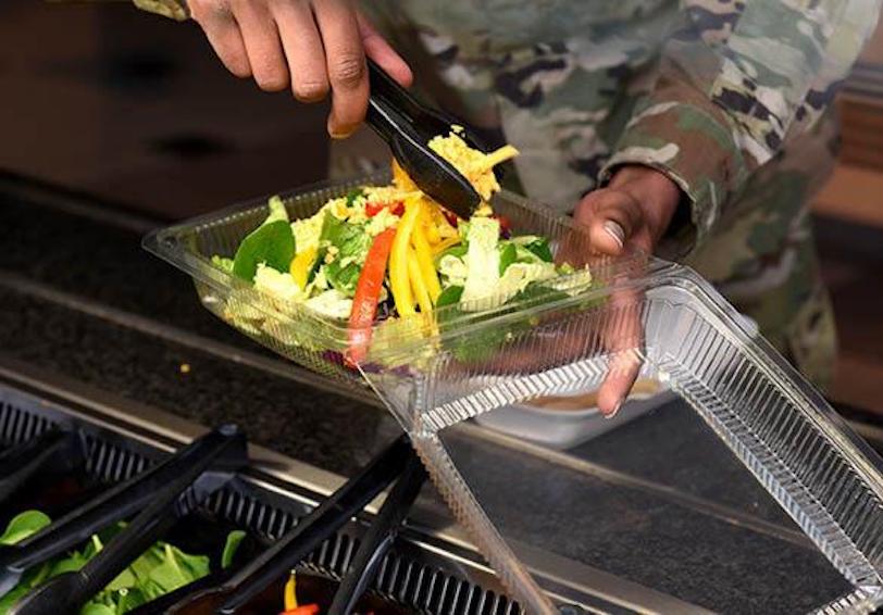 An airman fills a salad to-go box with a variety of fresh vegetables as part of his lunch