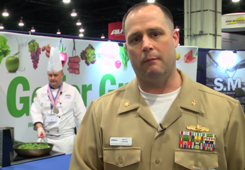 Still from video with sailor talking to camera and chef in background