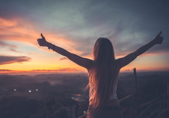 Woman looks at sunset and raises arms to embrace military wellness and performance optimization