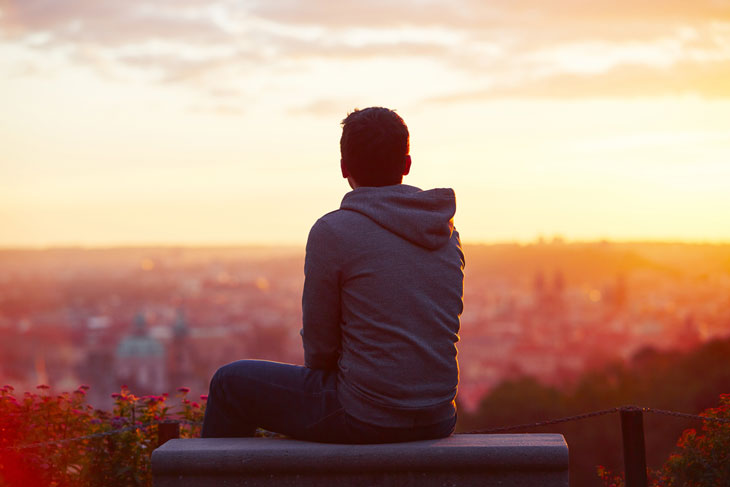 Person sitting on a bench looking over a city at sunset