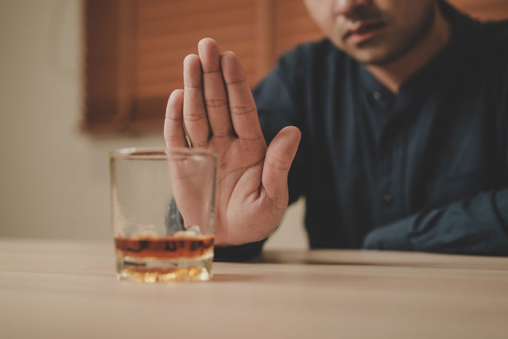 Individual holding up hand at a small cup of alcohol signaling to stop