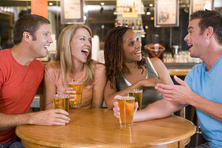 Group of friends talking and laughing at bar table together 