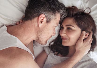 Couple lying in bed looking into each other's eyes emphasizing the importance of relationships and communication.