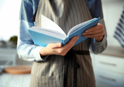 Person holding a cookbook refers to HPRC tips for optimizing performance and financial management with home-cooked meals  