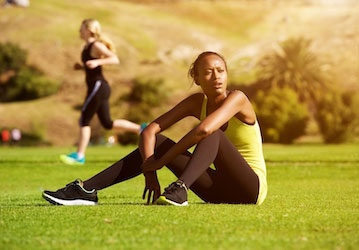 Woman in workout clothing sitting in grassy area catching her breath optimizes physical training with post-exercise  afterbur
