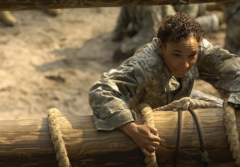 A Service Member pulls her way to the top of an obstacle during training showing her optimized military performance and total