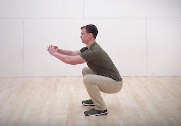 Man performing an air squat with correct form as part of a military workout to optimize fitness and prevent injury