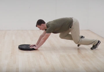 Man training for improved military fitness and injury prevention by pushing a weight across the gym floor 