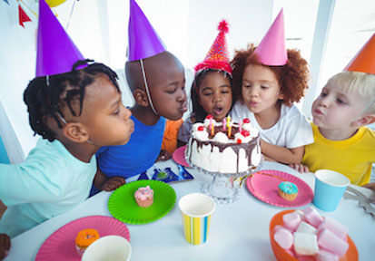 Group of kids wearing party hats and blowing out candles on a cake show how friendships promote healthy development and boost