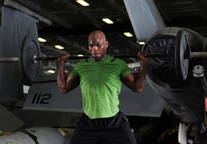 Man in green shirt lifts heavy weights during military workout and practices injury prevention strategies to train for perfor