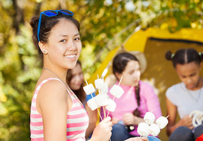 Girl holding marshmallows on stick in front of group of girls camping shows the benefit of social relationships for children 