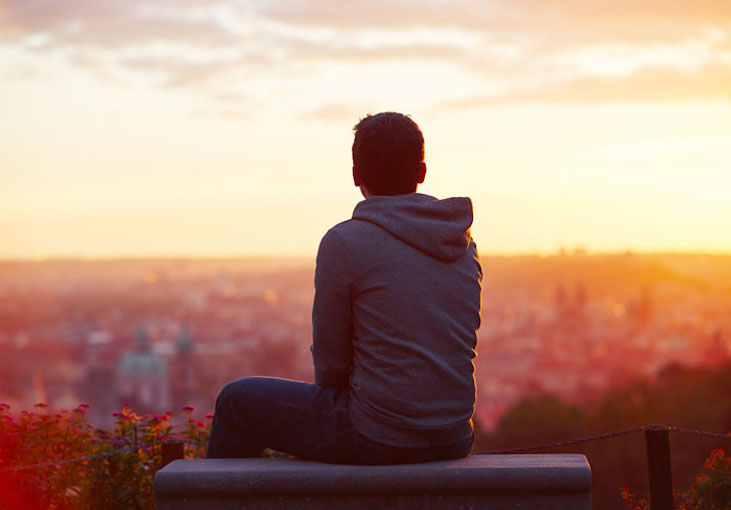 Person sitting on a bench looking over a city at sunset