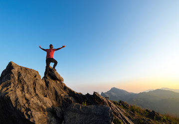 Person standing on mountain top accomplishes military workout with arms outstretched celebrating resilience and military fitn
