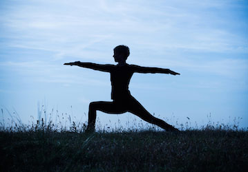 Silhouette of a person in a Warrior II yoga position working to increase flexibility in order to optimize physical fitness an