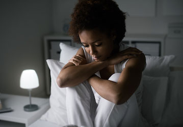 Sad looking woman sitting up in bed at night emphasizes need for HPRC stress management resources for improving rest  recover