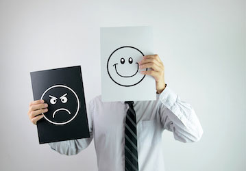 Man holding paper in front of his face with happy face and another piece of paper with an angry face off to the side optimize