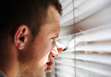 Man anxiously looking out window through blinds showing need for HPRC resources on mental health and resilience 