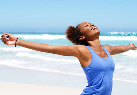 Smiling woman on beach with arms outstretched exhibiting positive mental health  improving wellness and stress management