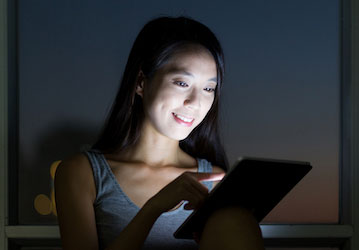 Woman in dark room working on tablet needs HPRC tips to reduce the effects of screen time for better sleep  physical and ment