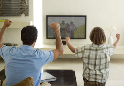 Father and son cheering while watching television together limit screen time during commercial breaks to boost healthy physic
