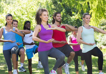 People doing tai chi outdoors for improved stress and pain management and holistic wellness. 