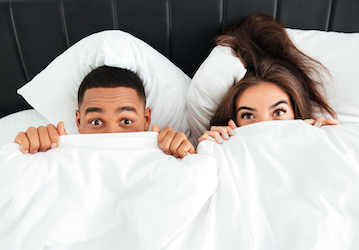 Couple in bed peeking out from blanket with surprised emotions practices communication in his relationship 