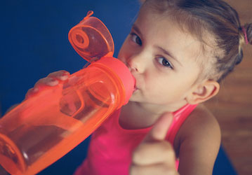 Young girl drinking from orange bottle showing wellness through proper fueling