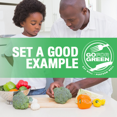 Set a Good Example. A man and child in a kitchen look at colorful vegetables on a cutting board and in a strainer.  Go for Green