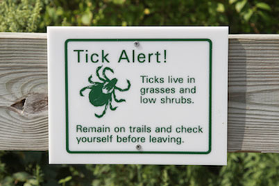 Sign reading: "Tick Alert! Ticks live in grasses and low shrubs. Remain on trails and check yourself before leaving."