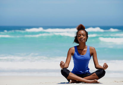 Woman meditating and breathing on a beach to build holistic wellness and promote stress management and resilience