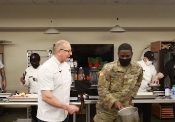 Chef Robert Irvine demonstrates proper cooking techniques with culinary specialists from the 1-2 Stryker Brigade Combat Team 