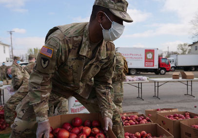 Service Members wears a mask and picks up a crate of food for military families to help fuel military wellness during coronav