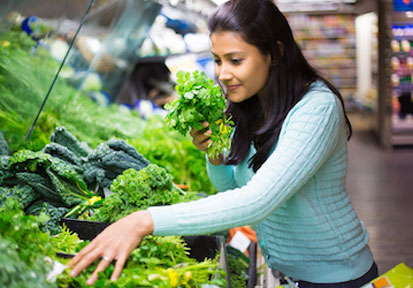 Woman in produce section of grocery store holds vegetables that aid in fueling holistic military wellness and performance nut