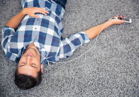 Man lying on floor listening to headphones with smartphone practices paced breathing for improved mental fitness and performa