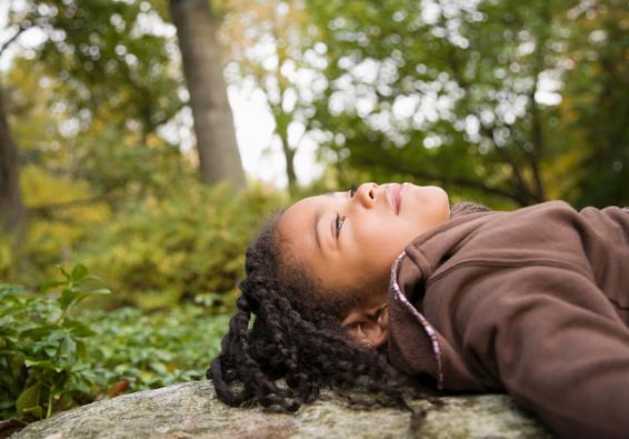 Girl laying back outside looking at the sky performs muscle relaxation exercises to manage stress and increase resilience  