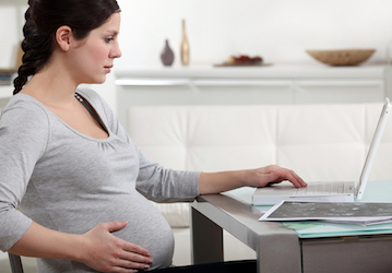 Pregnant woman sits at a desk in front of a laptop reading Coast Guard policy on pregnancy and maintaining military wellness 