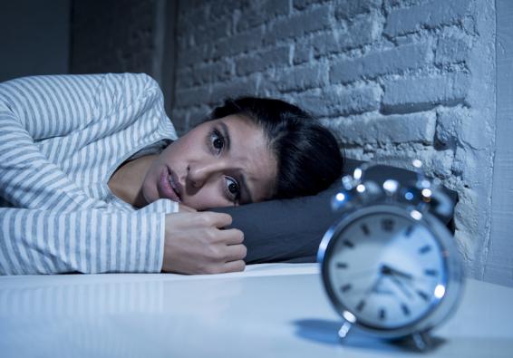 Anxious woman lying awake in bed and staring at the alarm clock needs HPRC strategies for better sleep and mental performance