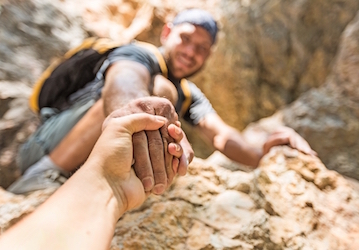 Man extending his hand to help another up a rocky hill strengthens resiliency through teamwork and support  