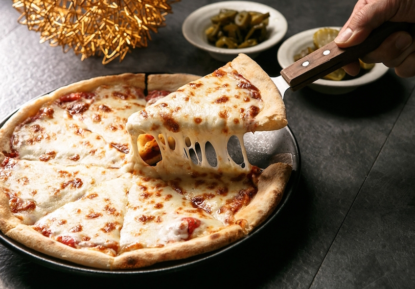 Spatula lifting one slice of cheese pizza from a whole pie highlights a need for healthier options for optimal nutrition and 